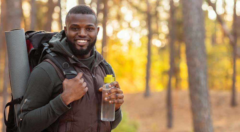 man with water bottle and backpack in woods