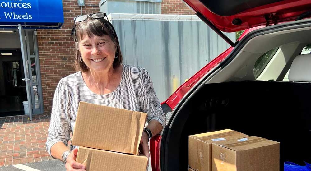woman holding boxes with trunk open and senior resources logo in background