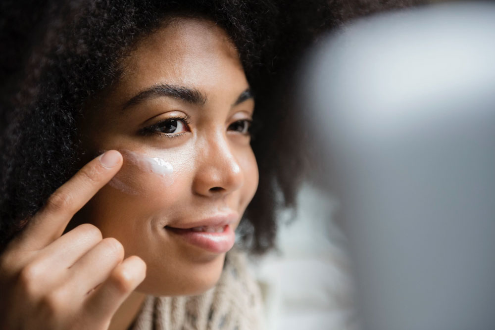 woman applying lotion to face in mirror