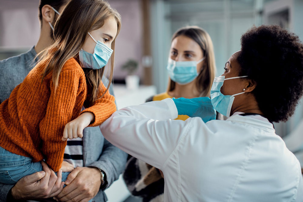 Little girl in mask bumping elbows with doctor in mask