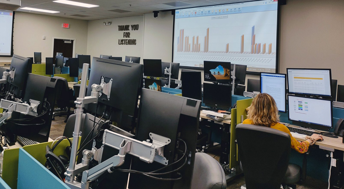 A woman seated at a desk, working intently in front of multiple computer screens.