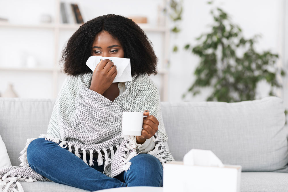 woman wrapped in blanket with tissue to her nose