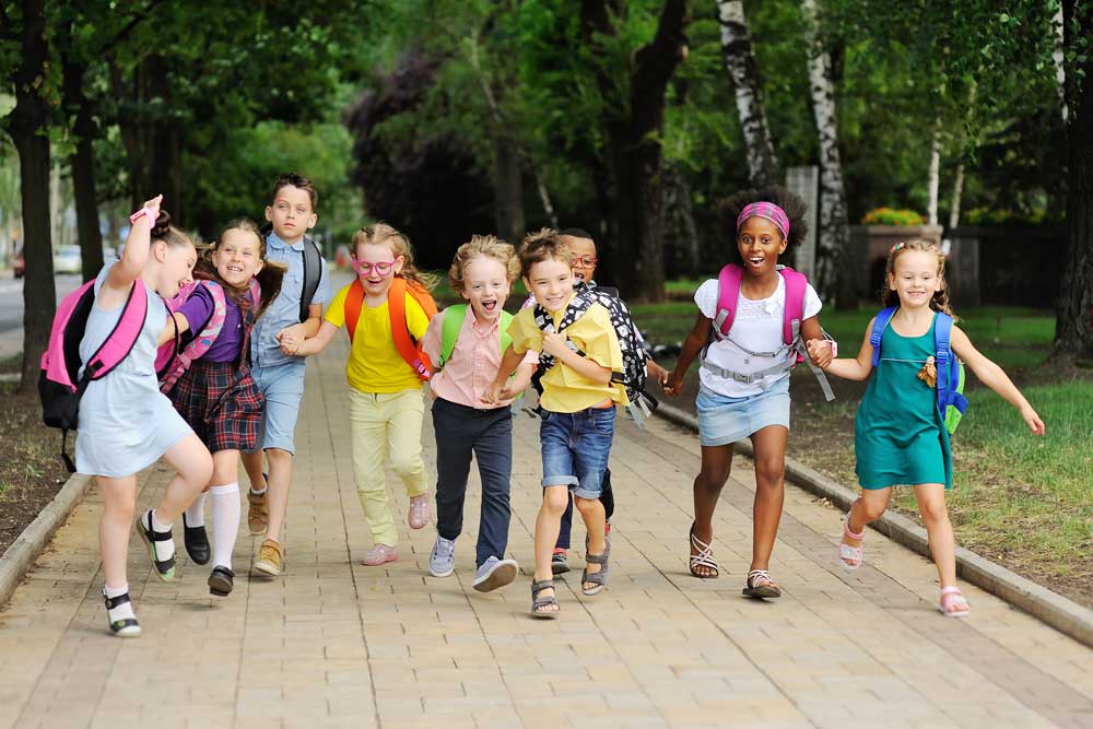 Group of kids with backpacks smiling and running on sidewalk
