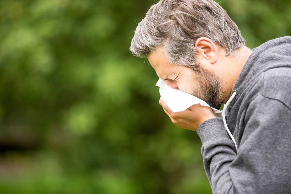 Man outside sneezing into tissue