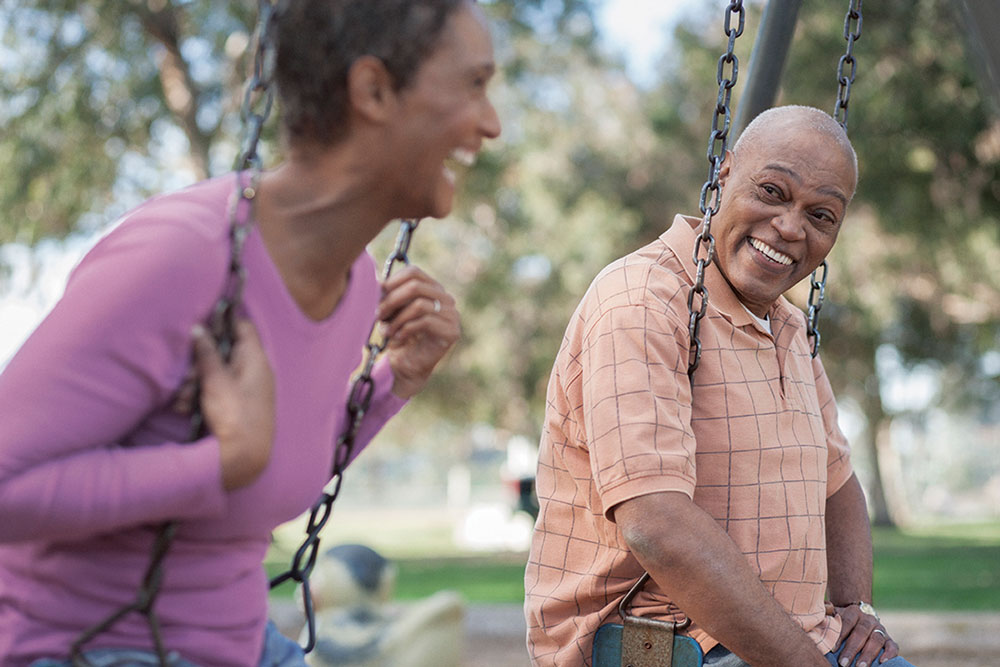 man and woman smile while sitting on swingset