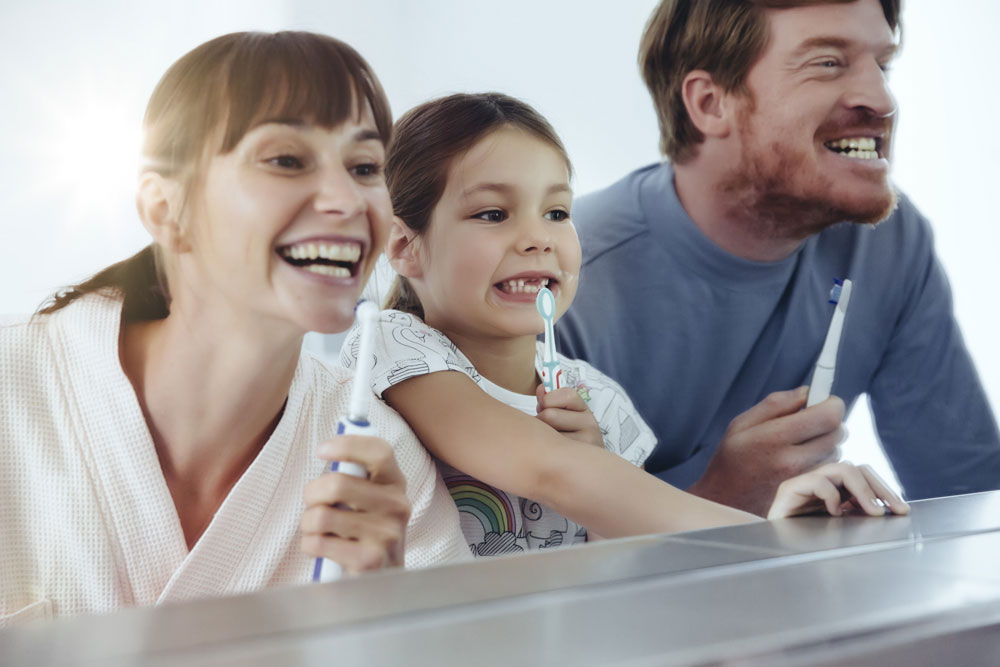 parents at little girl smile in mirror with toothbrushes
