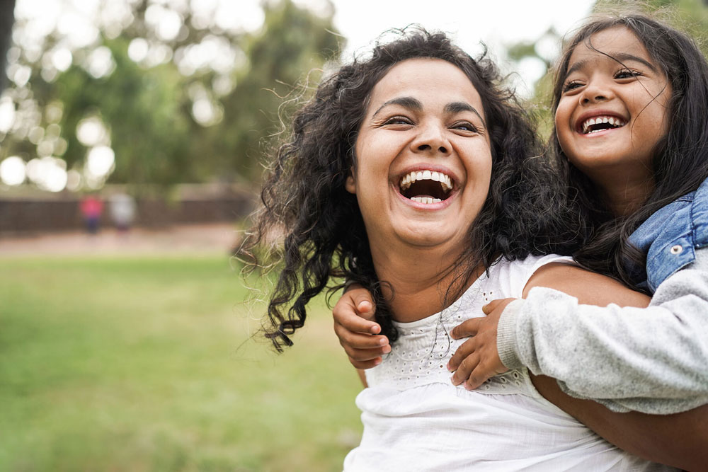 woman smiling with little girl on her back in park