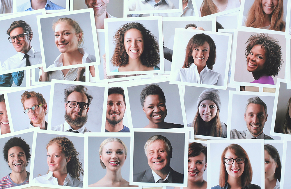 A variety of snapshots of people of multiple ethnicities, genders and ages are spread out over a surface.