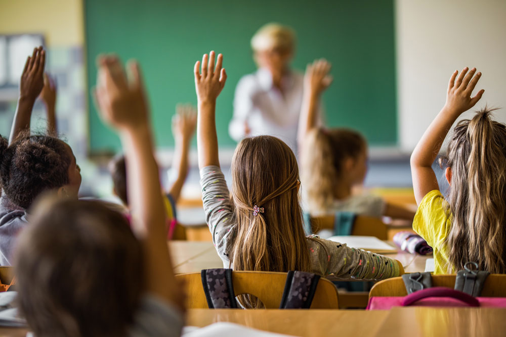 children in classroom with hands in the air