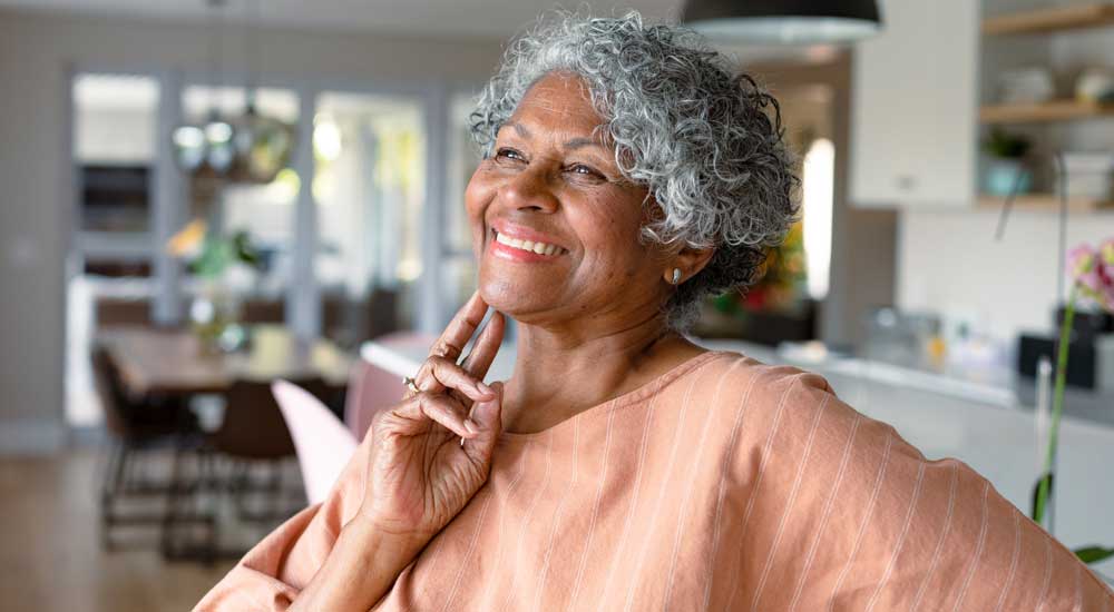 senior woman touching face, standing standing in kitchen