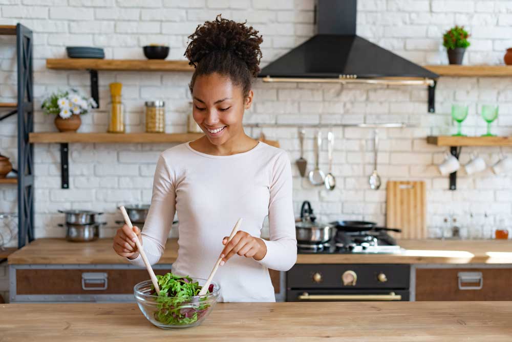 woman in kitchen making salad in bowl 