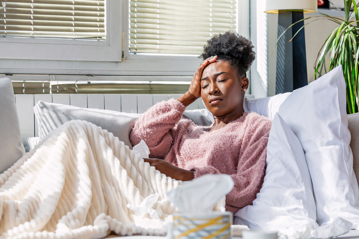 Woman on sofa with tissues holding her head