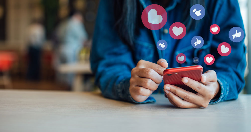 person holding phone in hands with hearts and like illustrations floating from phone
