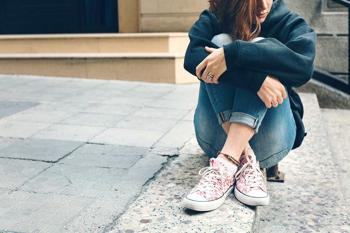 A teen sits on the ground with their knees drawn to their chest.